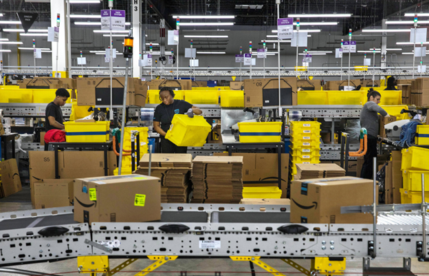 Amazon boxes going down a conveyor belt while employees pick and pack behind it. 