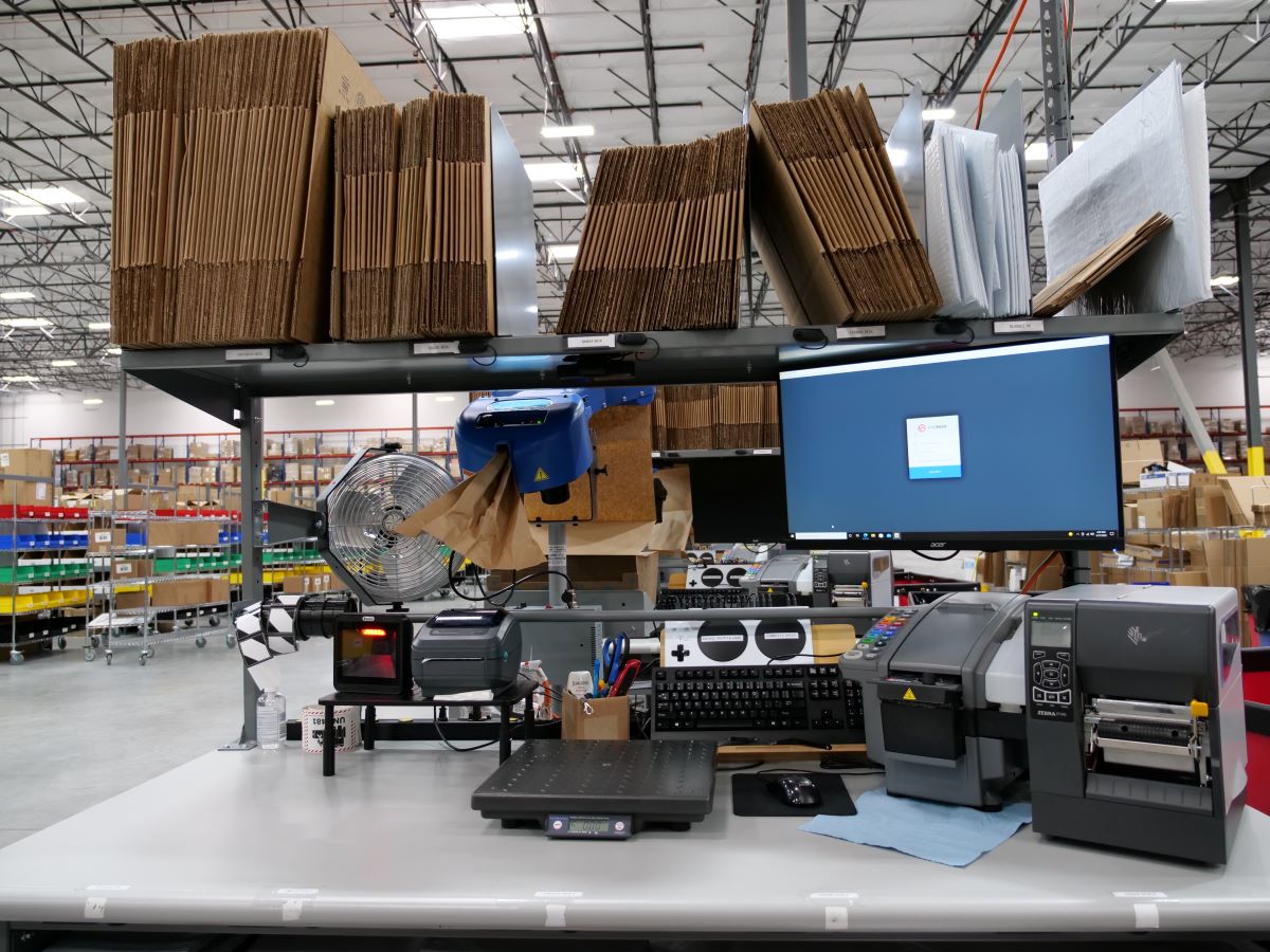 Warehouse packing station equipped with automation and one-touch buttons next to a computer screen.