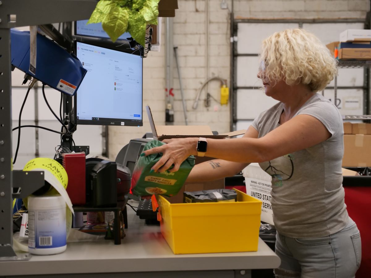 Woman packing multiple products into one box as she scans them into the warehouse management system