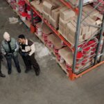 Three men talking and taking notes while they stand at the end of an aisle in a warehouse.