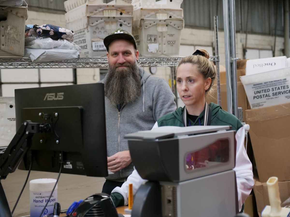 Two warehouse workers looking at a computer screen while scanning products in a warehouse.