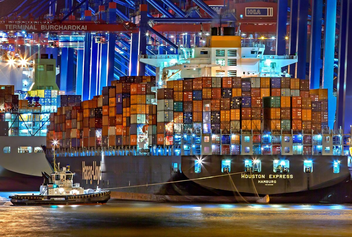 a large cargo ship backing into a port with hundreds of shipping containers on it.