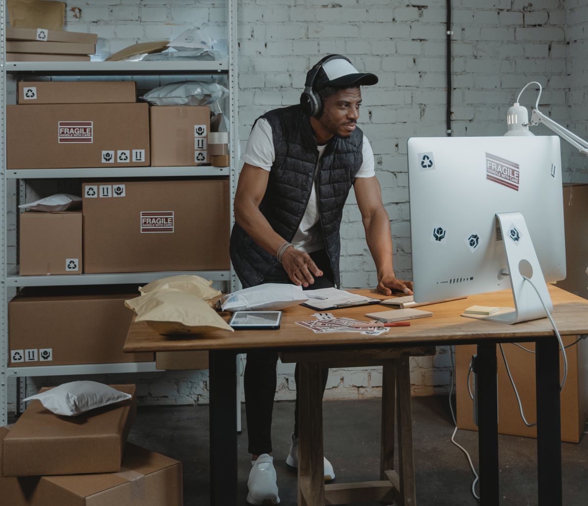 a man standing at a computer with boxes surrounding him.
